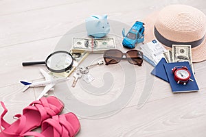 A piggy bank with dollar bills in a travel setting. In the composition of the image: Sun Hat, Alarm Clock. Concept of