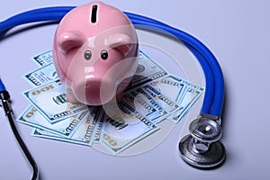 Piggy bank with dollar notes and stethoscope on a wooden desk