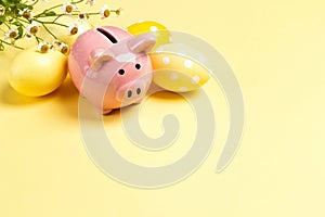 Piggy bank with eggs and daisies on a yellow background. Saving money for easter holidays