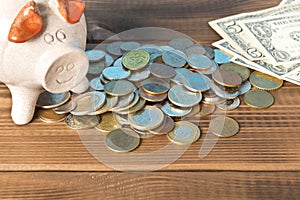 Piggy Bank and a few coins and dollar bills on the wooden table. Close up. The concept of saving money. Selective focus