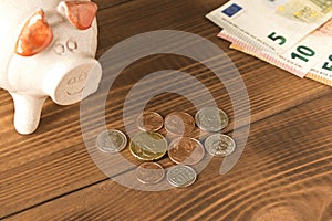 Piggy Bank and a few coins and Euro bills on the wooden table. Close up. The concept of saving money. Selective focus