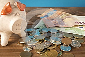 Piggy Bank and a few coins and euro bills on the wooden table. Close up. The concept of saving money. Selective focus