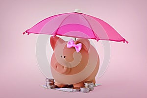 Piggy bank with hair bow and money under pink umbrella - Concept of woman, savings and and financial security