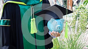 Piggy bank is holden by a person in graduated uniform. saving money for education, future investment concept