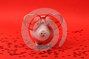 Piggy bank in love with red heart sunglasses standing on red background with shining red heart glitters photo