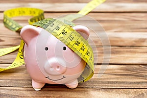 Piggy bank with measure tape on wooden background. Copy space