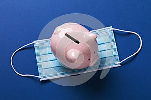 Piggy bank and medical mask on a blue background, top view