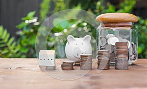 Piggy bank,money coins and house model on wood table with nature background on blue background,saving and investment concept