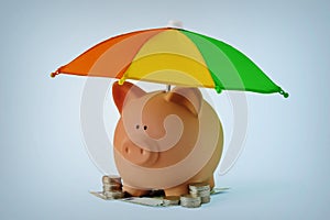 Piggy bank with money under rainbow umbrella - Concept of savings, money protection and financial security