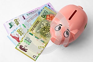 Piggy bank next to argentine pesos paper money on white background. Chanchito alcancÃÂ­a junto a billetes de pesos argentinos sobre photo