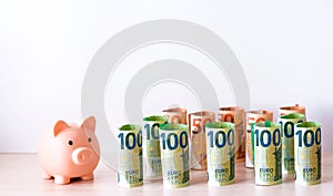 Piggy bank and paper money in denominations of 100 and 50 euros, folded into a roll, each bill is one. Free space. The concept of