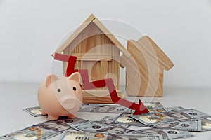 Piggy bank with red arrow down and wooden house models on dollar money, Saving or loan for buy house or real estate