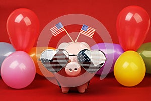 Piggy bank with retro sunglasses with USA flag and two small USA flags and balloons many colors on red background