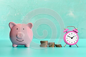 Between the piggy bank and a small pink alarm clock, three stacks of coins are in order. The symbol of the growth of