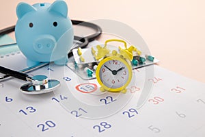 Piggy bank, stethoscope, alarm clock and calendar on a table, schedule to check up healthy concept