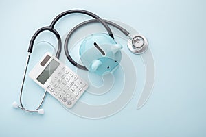 Piggy bank with stethoscope and calculator on blue background