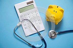 Piggy bank with stethoscope and calculator on the blue background
