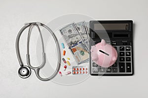 Piggy bank, stethoscope, calculator, money and pills on white textured table, flat lay. Medical insurance