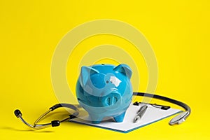 Piggy bank, stethoscope and clipboard on yellow background. Medical insurance