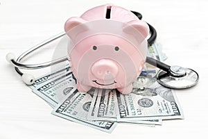 Piggy bank with stethoscope and money on white wooden table