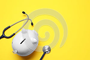 Piggy bank and stethoscope on yellow background, flat lay with space for text. Medical insurance