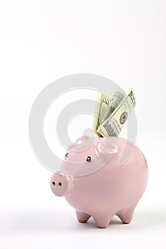 Piggy bank style money box with one hundred dollars falling into slot on a white studio background