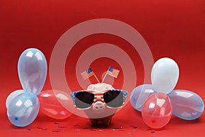 Piggy bank with sunglasses with USA flag and blue, red and white party balloons and two small USA flags on red background