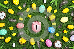 Piggy bank surrounded by eggs and Easter decoration on a green grass background