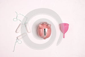 Piggy bank with tampons and menstrual cup on a white background. Save money with reusable feminine hygiene products