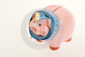 Piggy bank tied with measuring tape. Budget and squeezed savings concept. Investments and metering or counting