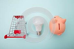 Piggy bank with trolley and lamp on blue background. Power savings concept. Top view