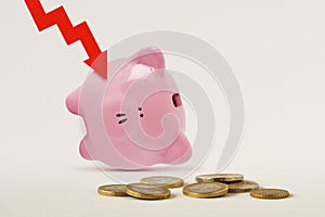 Piggy bank upside down with red arrow and coins - Concept of economy and financial crisis