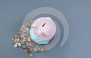 Piggy bank wearing medical mask with coins on gray desktop background