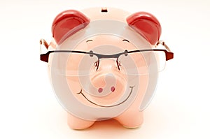 Piggy bank wearing reading glasses on white background.