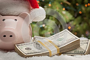 Piggy Bank Wearing Santa Hat Near Stacks of Hundred Dollar Bills on Snowflakes