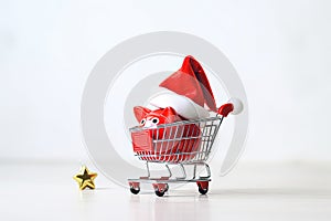 Piggy bank wearing Santa hat in shopping cart on white background. Christmas shopping concept