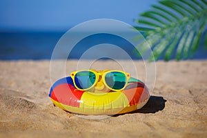 Piggy bank wearing sunglasses and floating ring on sandy beach