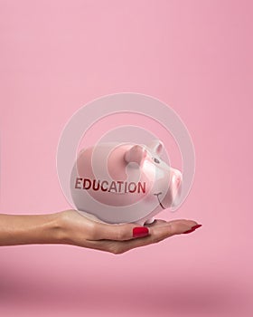 Piggy bank in a woman hand with inscription EDUCATION on a pink background. Minimal saving money concept