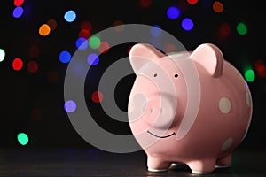 Piggy bank on wooden table against blurred Christmas lights