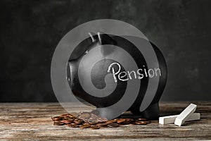 Piggy bank with word PENSION, chalk and coins on table