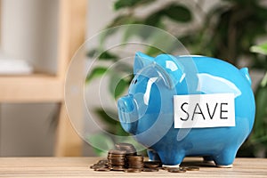 Piggy bank with word SAVE and coins on table against blurred background