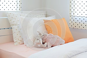 Piggy and rabbit doll setting on bed next to orange color pillow