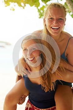 Piggybacks on the beach. Portrait of an attractive young woman piggybacking her friend on the beach.