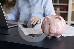 Piggybank on desk, woman use computer and calculator on background