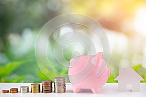 Piggybank of money with coins stack stair step up growing saving money for house with green nature and bokeh background.