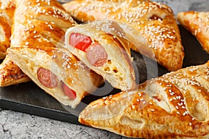 Pigs in blankets puff pastry turnover with sausage, cheese and pepper close-up on a marble board. Horizontal