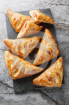 Pigs in blankets puff pastry turnover with sausage, cheese and pepper close-up on a marble board. Vertical top view