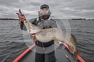 Pike fishing. Happy fisherman with big fish trophy at the boat with tackles