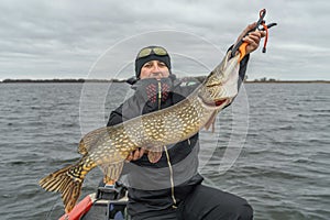 Pike fishing. Happy fisherman with big fish trophy at the boat with tackles