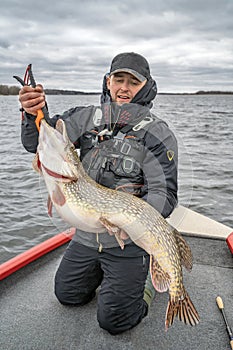 Pike fishing. Happy fisherman with big fish trophy at the boat with tackles